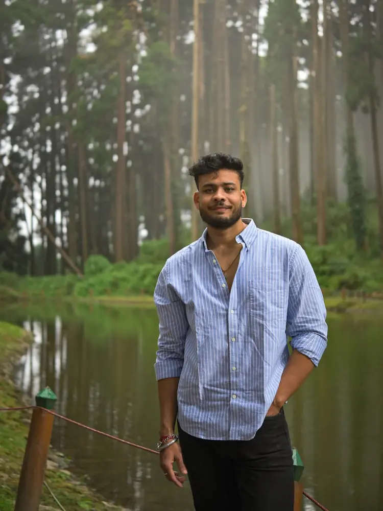 Mayukh standing by a misty lake with tall pine trees behind him
